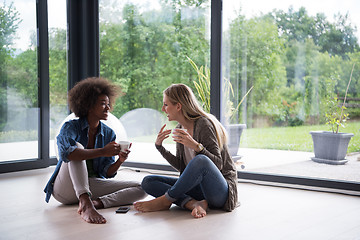 Image showing multiethnic women sit on the floor and drinking coffee