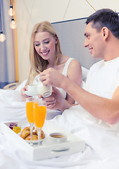 Image showing smiling couple having breakfast in bed in hotel