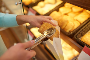 Image showing hand with tongs taking bun at bakery or grocery