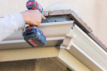 Image showing Worker Attaching Aluminum Rain Gutter to Fascia of House.