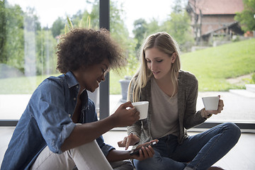 Image showing multiethnic women sit on the floor and drinking coffee