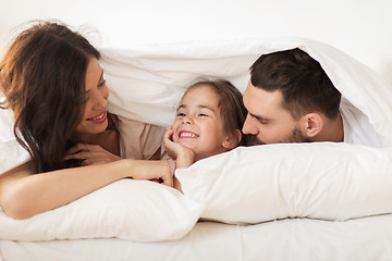 Image showing happy family lying in bed under blanket at home