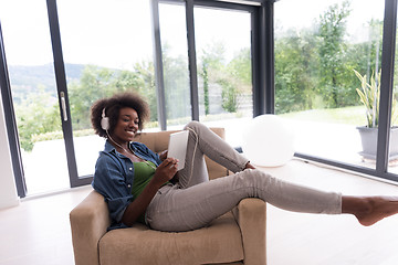 Image showing African american woman at home in chair with tablet and head pho