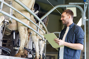 Image showing man with clipboard and milking cows on dairy farm