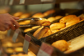 Image showing hand with tongs taking bun at bakery or grocery