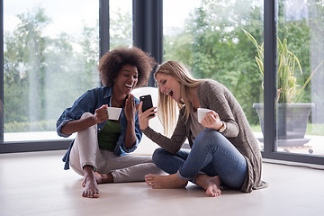 Image showing multiethnic women sit on the floor and drinking coffee