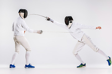 Image showing The two men wearing fencing suit practicing with sword against gray