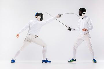 Image showing The two men wearing fencing suit practicing with sword against gray