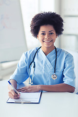 Image showing happy female doctor or nurse writing to clipboard