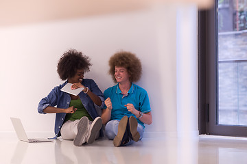 Image showing multiethnic couple sitting on the floor with a laptop and tablet