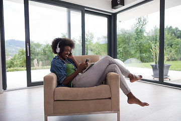 Image showing African american woman at home in chair with tablet and head pho