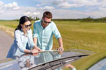 Image showing happy man and woman with road map on car hood