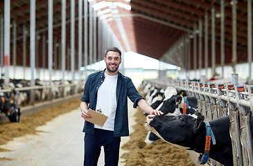 Image showing farmer with clipboard and cows in cowshed on farm