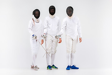 Image showing The two men and woman wearing fencing suit with sword against gray