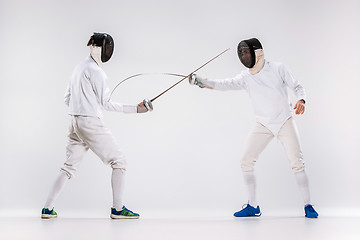 Image showing The two men wearing fencing suit practicing with sword against gray