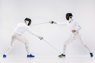 Image showing The two men wearing fencing suit practicing with sword against gray