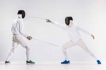 Image showing The two men wearing fencing suit practicing with sword against gray