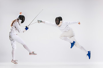 Image showing The men and woman wearing fencing suit practicing with sword against gray