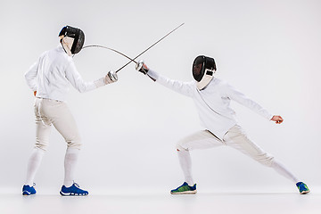 Image showing The two men wearing fencing suit practicing with sword against gray