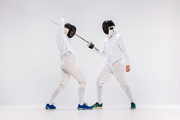 Image showing The two men wearing fencing suit practicing with sword against gray