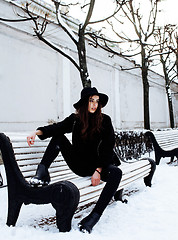 Image showing young pretty modern hipster girl waiting on bench at winter snow park alone, lifestyle people concept 
