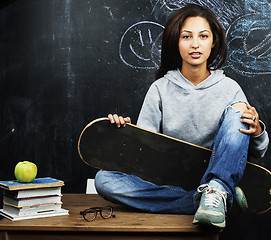 Image showing young cute teenage girl in classroom at blackboard seating on ta