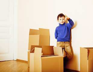 Image showing little cute boy in empty room, remoove to new house. home alone emong boxes close up kid smiling