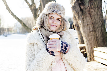 Image showing young pretty teenage hipster girl outdoor in winter snow park having fun drinking coffee, warming up happy smiling, lifestyle people concept