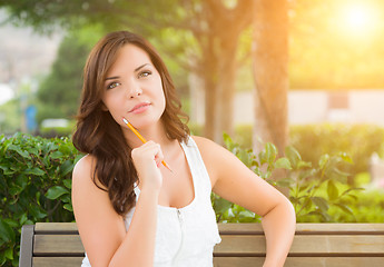 Image showing Young Adult Female Student with Pencil on Bench Outdoors