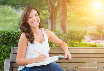 Image showing Young Adult Female Student with Pencil on Bench Outdoors