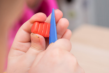 Image showing The child cuts off a piece of a stack of red clay