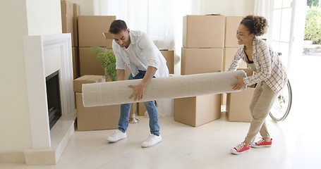 Image showing Young couple carrying a rolled rug into a house