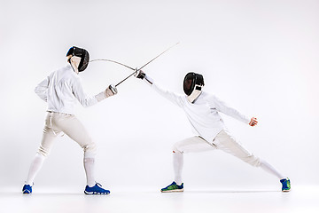 Image showing The two men wearing fencing suit practicing with sword against gray