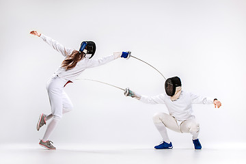 Image showing The woman and man wearing fencing suit practicing with sword against gray