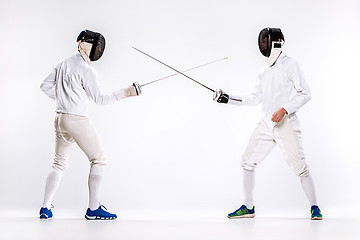 Image showing The two men wearing fencing suit practicing with sword against gray