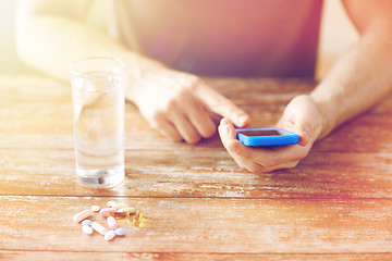 Image showing close up of hands with smartphone, pills and water