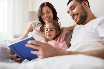Image showing happy family reading book in bed at home