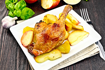 Image showing Duck leg with apple and basil in plate on dark board