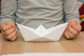Image showing On the table in front of the girl is a paper boat