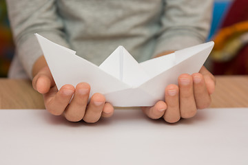 Image showing A child holding a white boat made of paper