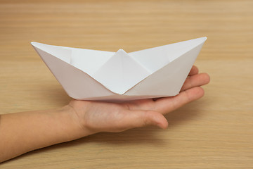 Image showing On the hand of the child is a paper boat on the desktop background