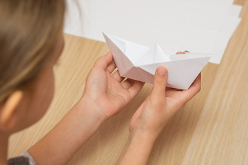 Image showing A girl looks at a paper boat made by hand