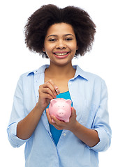 Image showing happy african woman putting coin into piggy bank