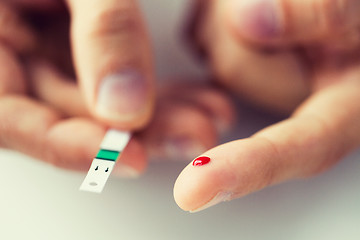 Image showing close up of male finger with blood and test stripe