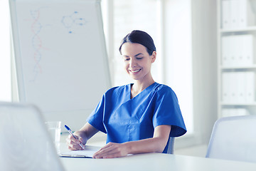 Image showing happy female doctor or nurse writing to clipboard