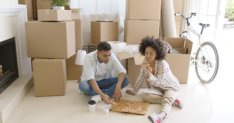 Image showing Hungry young couple eating a pizza on the floor