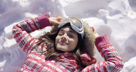 Image showing Young woman lying on snow with ski goggles