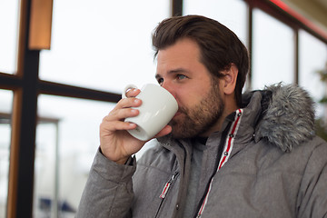 Image showing Thoughtful man wearing warm winter jacket looking out the window and drinking coffee.