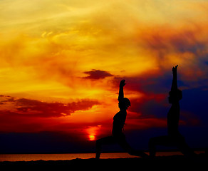 Image showing Yoga people training and meditating in warrior pose outside by beach at sunrise or sunset.