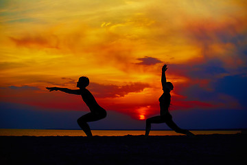 Image showing Yoga people training and meditating in warrior pose outside by beach at sunrise or sunset.